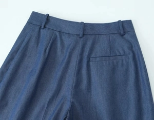Detail of dark blue denim pants showing the waistband and back welt pocket stitching