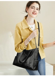 Detailed view of a black glossy leather tote bag with adjustable strap and dual handles