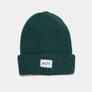 Close-up of thick rib-knit texture and white AQER fabric label on dark green beanie