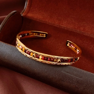 Detailed macro view of gold plated open bangle with colorful stone beads in a velvet box