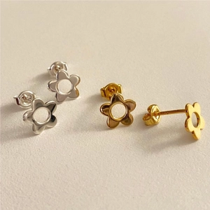 Close-up of gold and silver flower stud earrings with hollow petal design on white