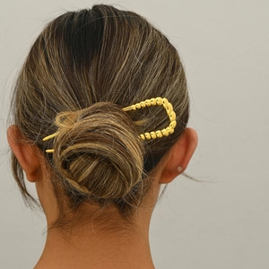 Golden U-shaped metal hair pin with textured beads shown on a model's elegant bun