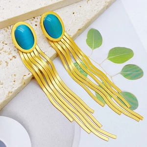 Detailed view of long gold tassel earrings with turquoise oval stones on marble background