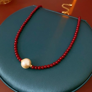 Gros plan du collier de perles rouges avec perle centrale et fermoir doré sur boîte