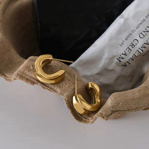 Minimalist gold C-shaped thick hoop earrings with polished mirror finish on kraft paper