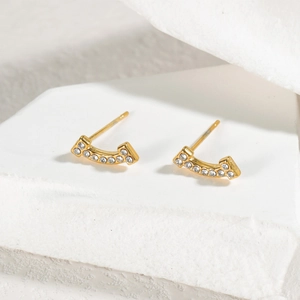 Macro detail of gold-plated curved smile earrings with crystals on white stone surface