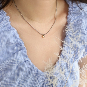 Minimalist silver bead chain necklace with polished gold heart pendant on a model