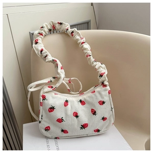 Detail of strawberry print corduroy bag with pleated scrunchie strap on white books