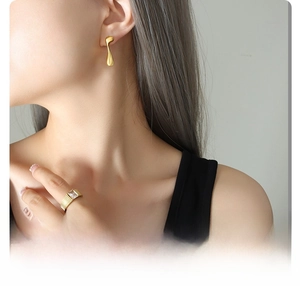 Primer plano de pendientes de titanio bañados en oro de 18K y anillo con gema en modelo