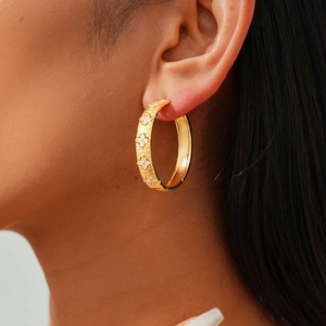 Macro detail of 18k gold plated hoop earring with zircon flower charms and brushed texture
