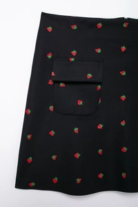 Détail d'une jupe en sergé noir avec broderie de fraise rouge et une poche à rabat