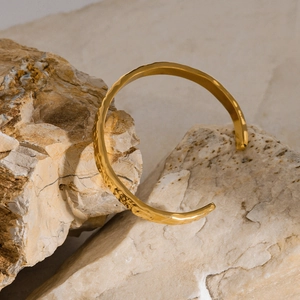 Detail view of gold wave texture bangle displayed on a natural raw stone background