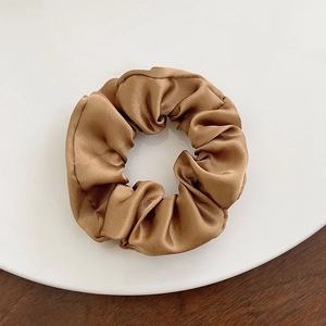 Detail of golden satin scrunchie with silk texture on white plate and wooden surface