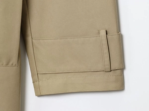 Dettaglio del trench kaki che mostra il tessuto twill e il cinturino regolabile sulla manica