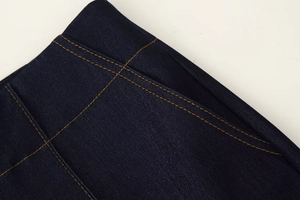 Détail du tissu denim bleu foncé avec coutures contrastées jaunes à la taille