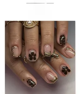 Detalle de uñas postizas cuadradas cortas con arte floral marrón y bordes dorados en 3D