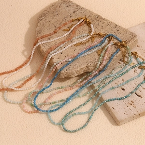 Close-up of colorful beaded necklaces with 18K gold plated clasps on beige stone props