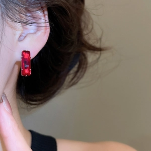 Close-up of elegant rectangular red zircon stud earring worn on model ear with silver claw