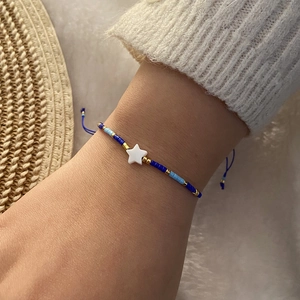 Close-up of blue beaded bracelet with white shell star charm on wrist