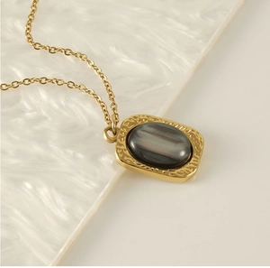 Close-up of hammered gold square pendant with iridescent oval stone inlay on white tray