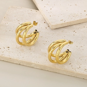 Close-up of golden triple-layered C-shaped hoop earrings on beige travertine blocks