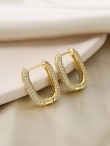 Macro detail of U-shaped gold earrings with paved zircon stones on satin background