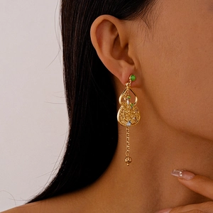 Close-up of golden gourd earring with green bead on model in neo-Chinese style