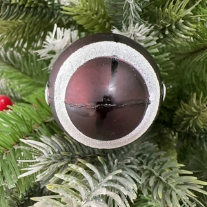 Close-up of deep red Christmas ball ornament with silver glitter rings on pine branch