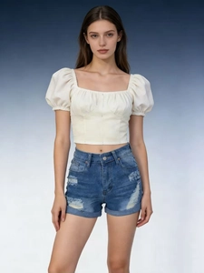Detail of high-waist ripped denim shorts paired with a cream puff-sleeve crop top