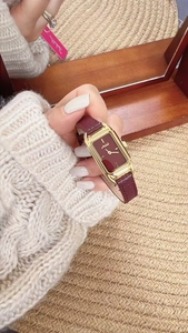 Close-up of vintage rectangular gold watch with burgundy leather strap on wrist