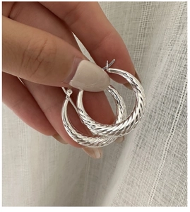 Nahaufnahme von S925 Silber-Creolen mit gedrehtem Croissant-Muster in der Hand gehalten