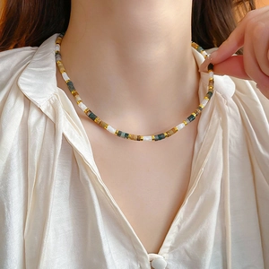Detail of beaded necklace with gold accents worn over a white silk shirt for a luxury look