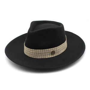 Detailed close-up of a black wide-brim fedora hat featuring a gold M logo buckle detail