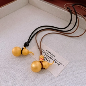 Close-up of matte gold gourd pendants with red enamel on woven leather cords