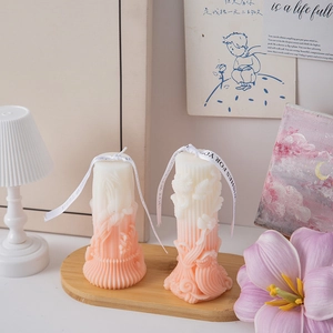 Detail of two-pack gradient pink Roman pillar candles with floral relief and white ribbon