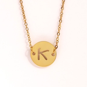 Gros plan du pendentif pièce dorée avec lettre K sur une fine chaîne en acier inoxydable