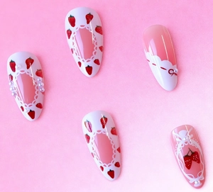 Detail of pink almond fake nails with strawberry print, red bows and tiny pearl accents