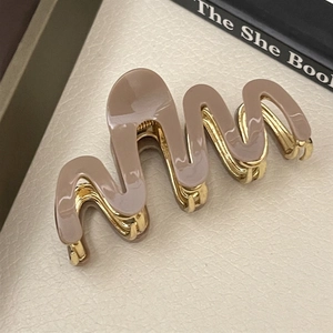 Detail showing wavy coffee acetate hair claw clip with golden metal teeth on leather surface