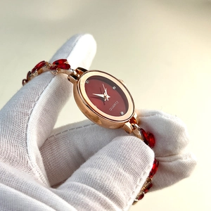 Detail of luxury oval gold bracelet watch with red dial and gemstone inlays