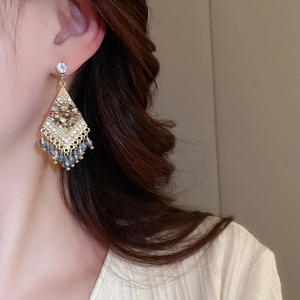 Close-up of diamond-studded geometric tassel earrings worn by a model in warm light