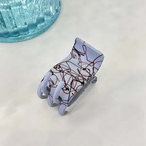 Détail d'une pince à cheveux mate bleu-gris avec motif abstrait brun et design à 6 dents