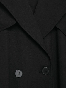 Detail of black trench dress showing twill fabric texture and matte button closure
