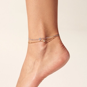 Detail shot of a layered gold and silver anklet with zircon pendants on a model