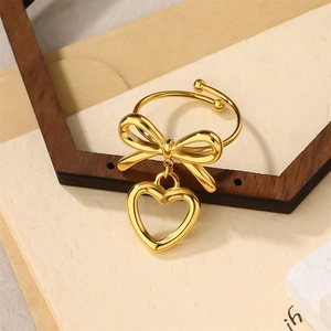 Elegant gold bow ring with hollow heart pendant on a wooden frame background