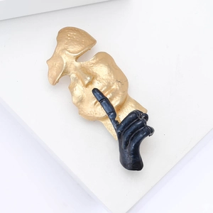 Broche masque doré artistique avec geste de main noire et texture martelée vintage