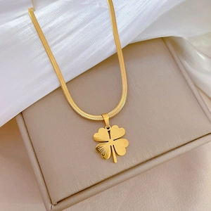 Macro detail of golden clover pendant with snake chain on soft silk background