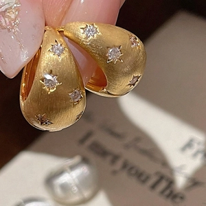 Macro shot of brushed gold star earrings with sparkling zircon inlay for women
