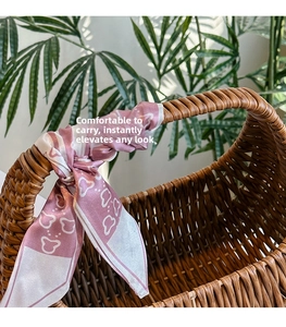 Detail of a pink floral silk scarf wrapped around the woven rattan handle of a stylish basket bag