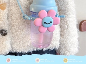 Close-up of cute cartoon flower straw cup with blue lid and adjustable strap on white coat