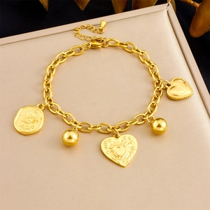 Detail of gold chain bracelet with heart and rose engraved pendants on textured background